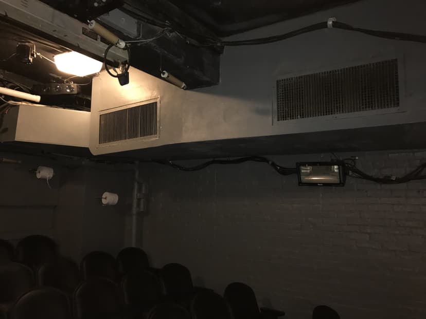 Dimly lit theater with black chairs, air vents, and exposed wiring on the dark gray walls, showcasing an example of intricate HVAC duct work.