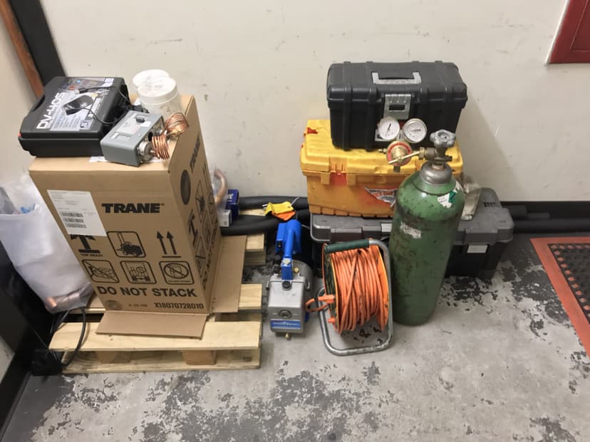 Pallet with various commercial HVAC equipment, including a green gas cylinder, coiled orange cable, toolboxes, and boxes labeled Trane.