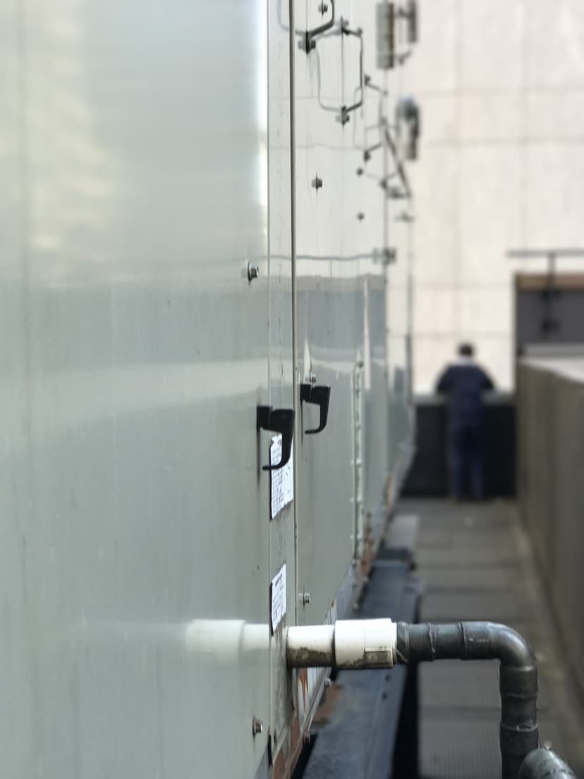 A person in the distance, standing next to a large industrial unit with pipes and handles on a rooftop, takes in the rooftop scenery.
